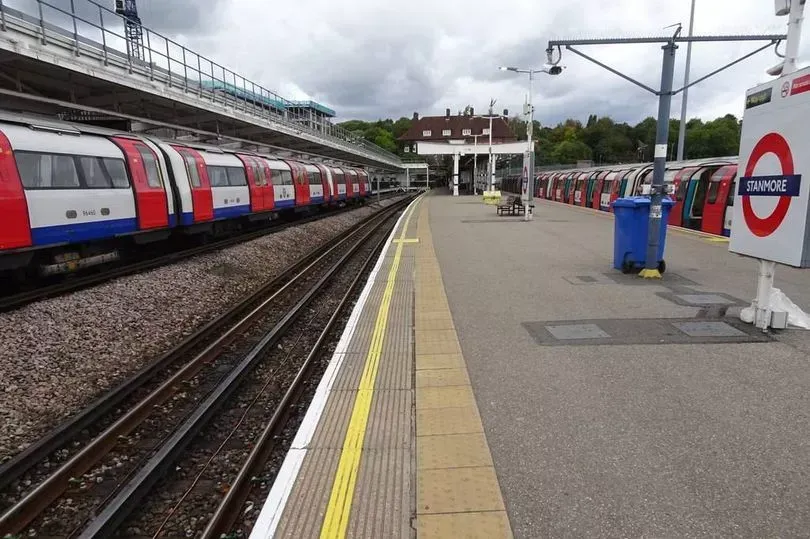 London Underground train at a station. Red and white train. Platform, tracks, blue bin.