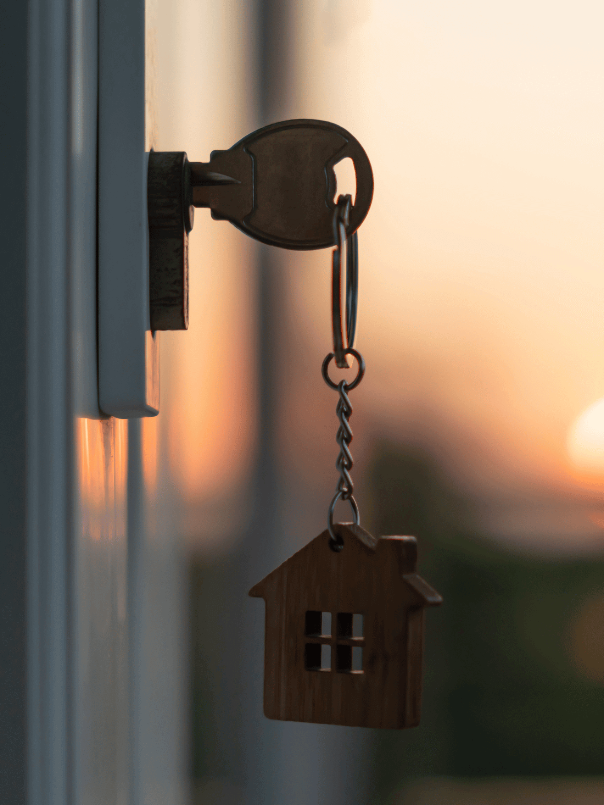 Key in a lock with a house-shaped keychain; a warm sunset is in the background.