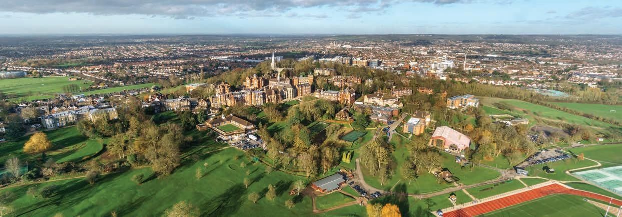 Aerial view of a cityscape with a large, ornate building complex on a hill surrounded by green fields and trees.