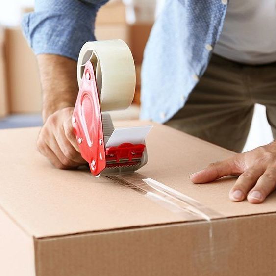 Person sealing a cardboard box with tape, likely preparing for moving or shipping.