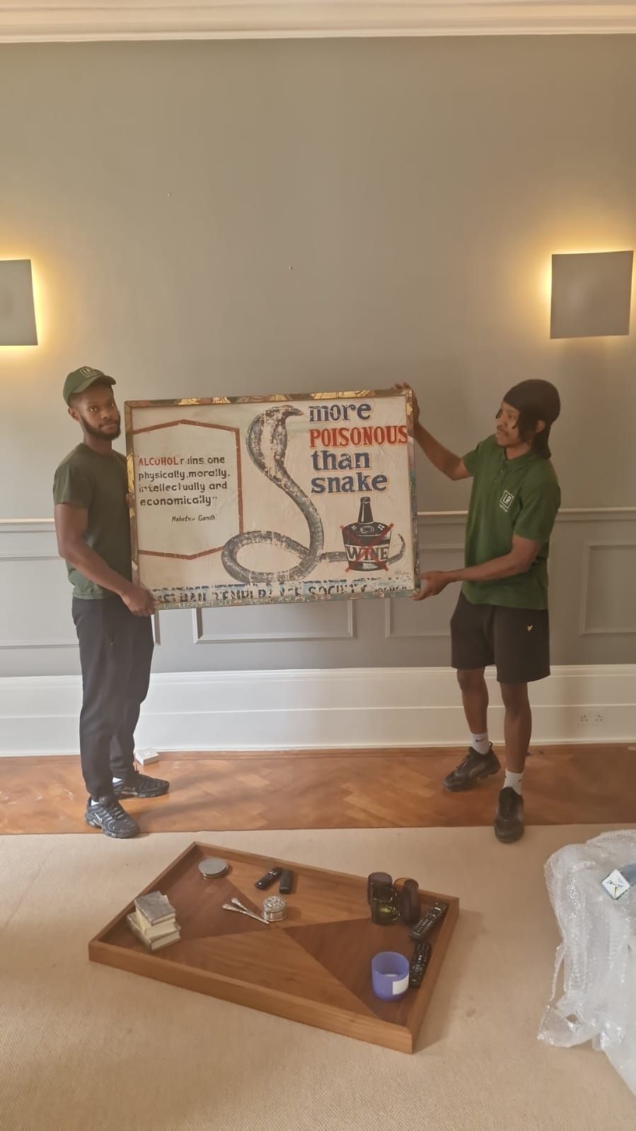 Two movers in a room holding a large sign depicting a cobra and text. The setting is a room with a wooden floor