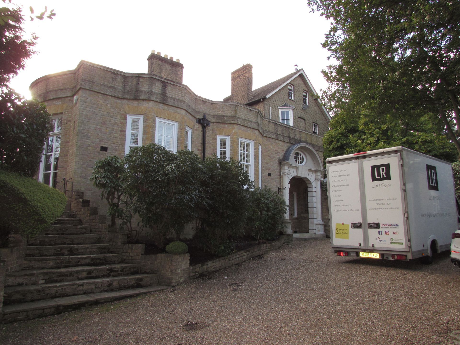 A light-colored brick house with a gray stone staircase and a large white truck parked in front of it.