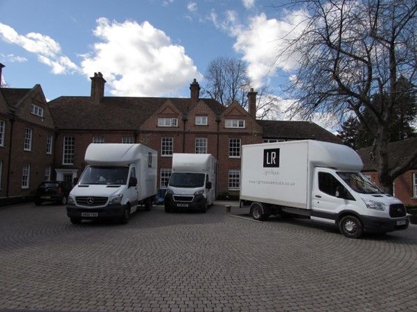 Three white delivery vans parked in front of a brick building under a cloudy sky.