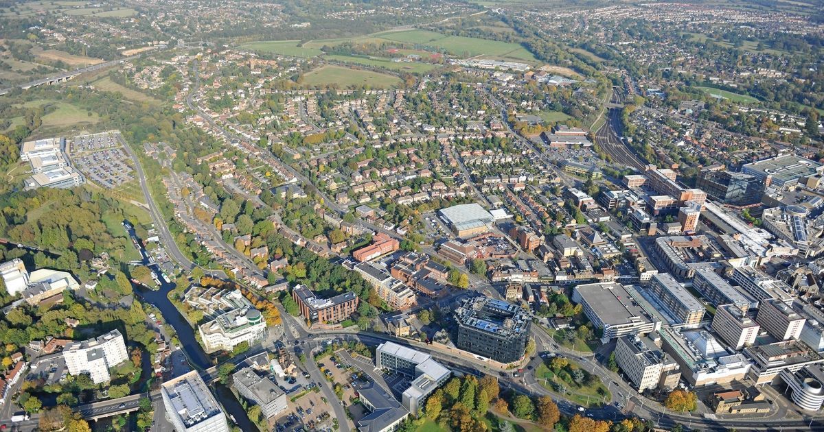 Aerial view of a town with buildings, roads, and green spaces under a sunny sky.
