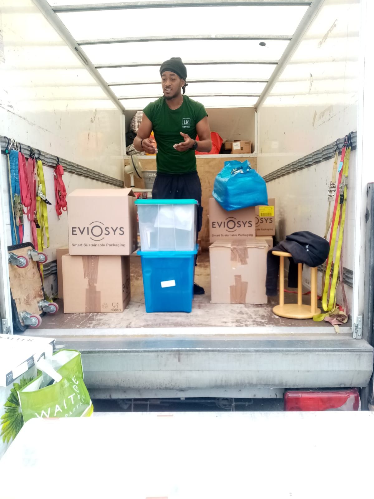 Man inside a moving truck surrounded by packed boxes and belongings. He is gesturing as if explaining or directing.