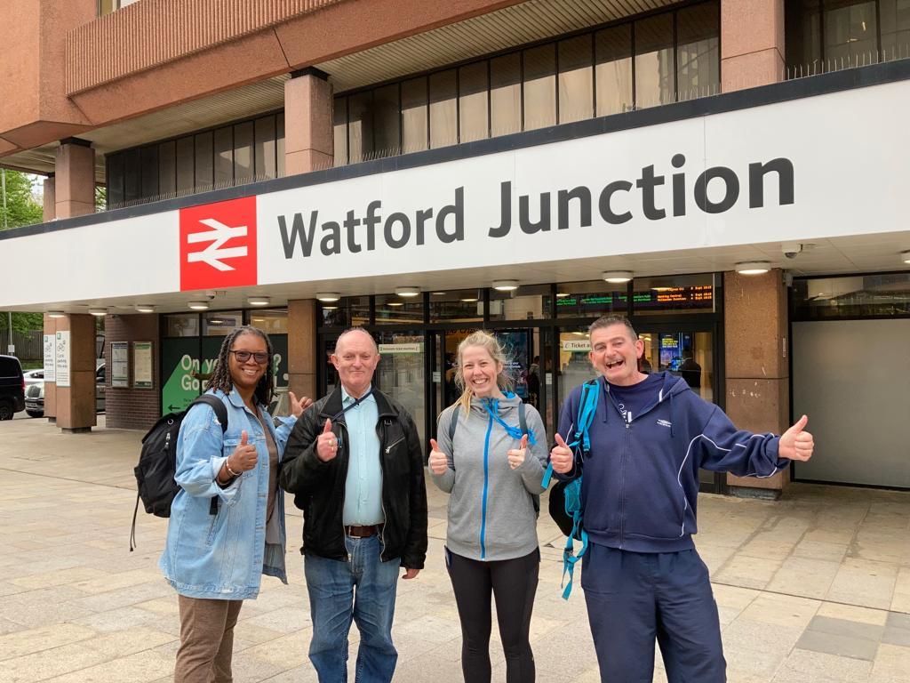 Stone cottages line a river in a Cotswold village, a small bridge in the foreground reflecting the colorful sunset sky.