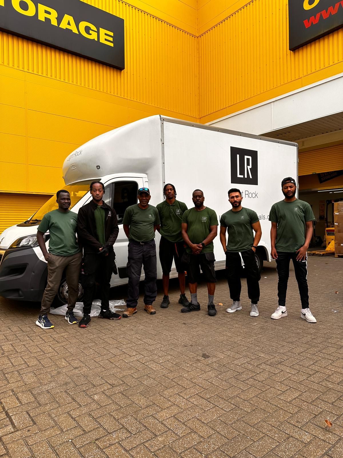 Seven men in green shirts and dark pants stand in front of a white box truck with