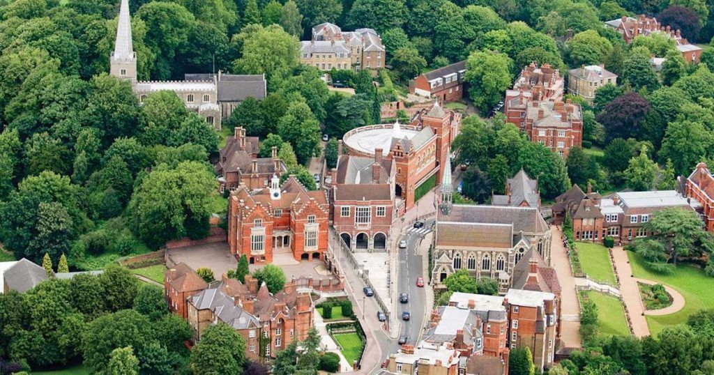Aerial view of a historic town with red-brick buildings, green trees, and a church steeple.