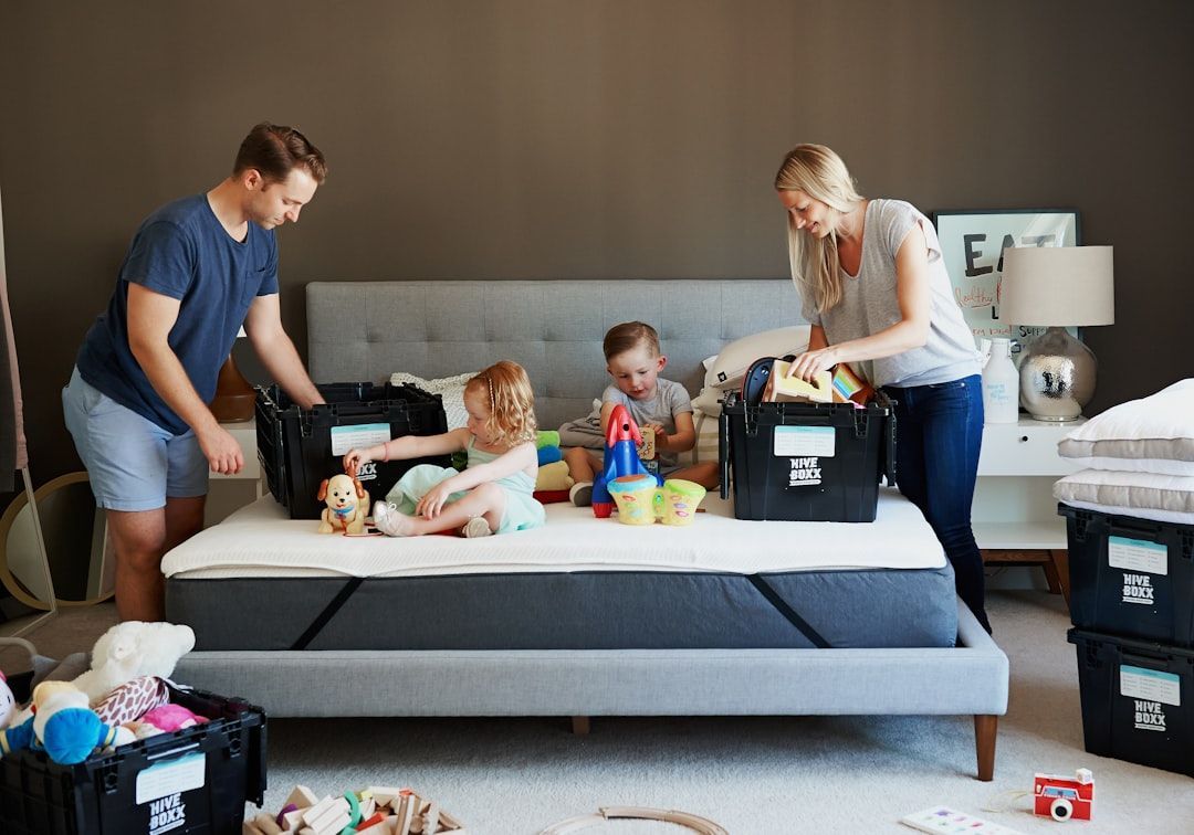 Family unpacking boxes on a bed in a bedroom. Toys and bedding are visible.