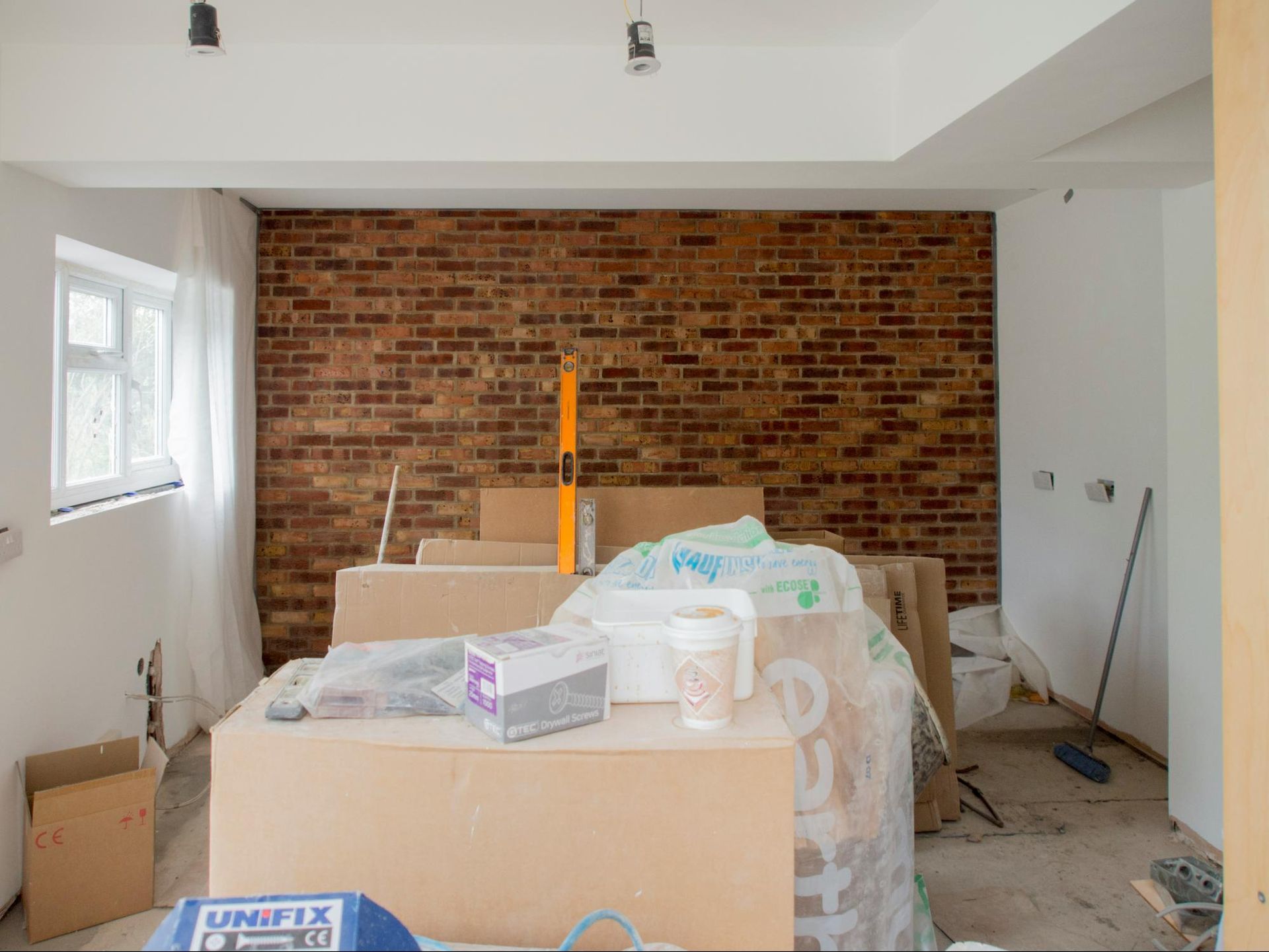 Interior room under construction, featuring brick accent wall, white walls, and construction materials.