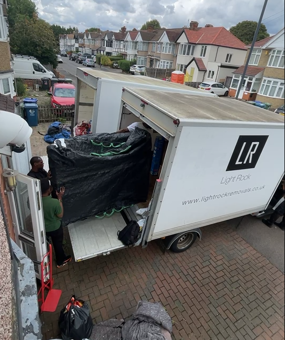 People loading a large, covered item into a white trailer labeled