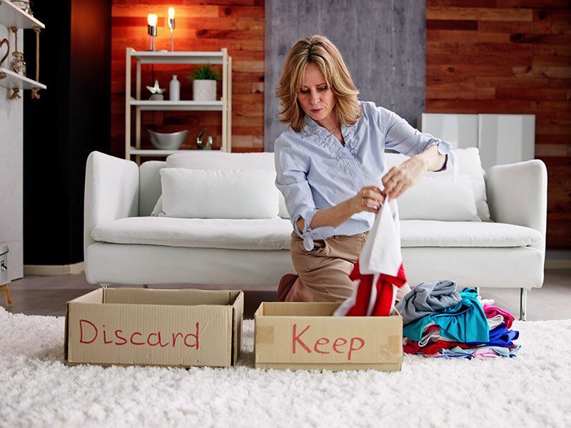 Woman sorting clothes on a rug in front of a couch, placing items in boxes labeled