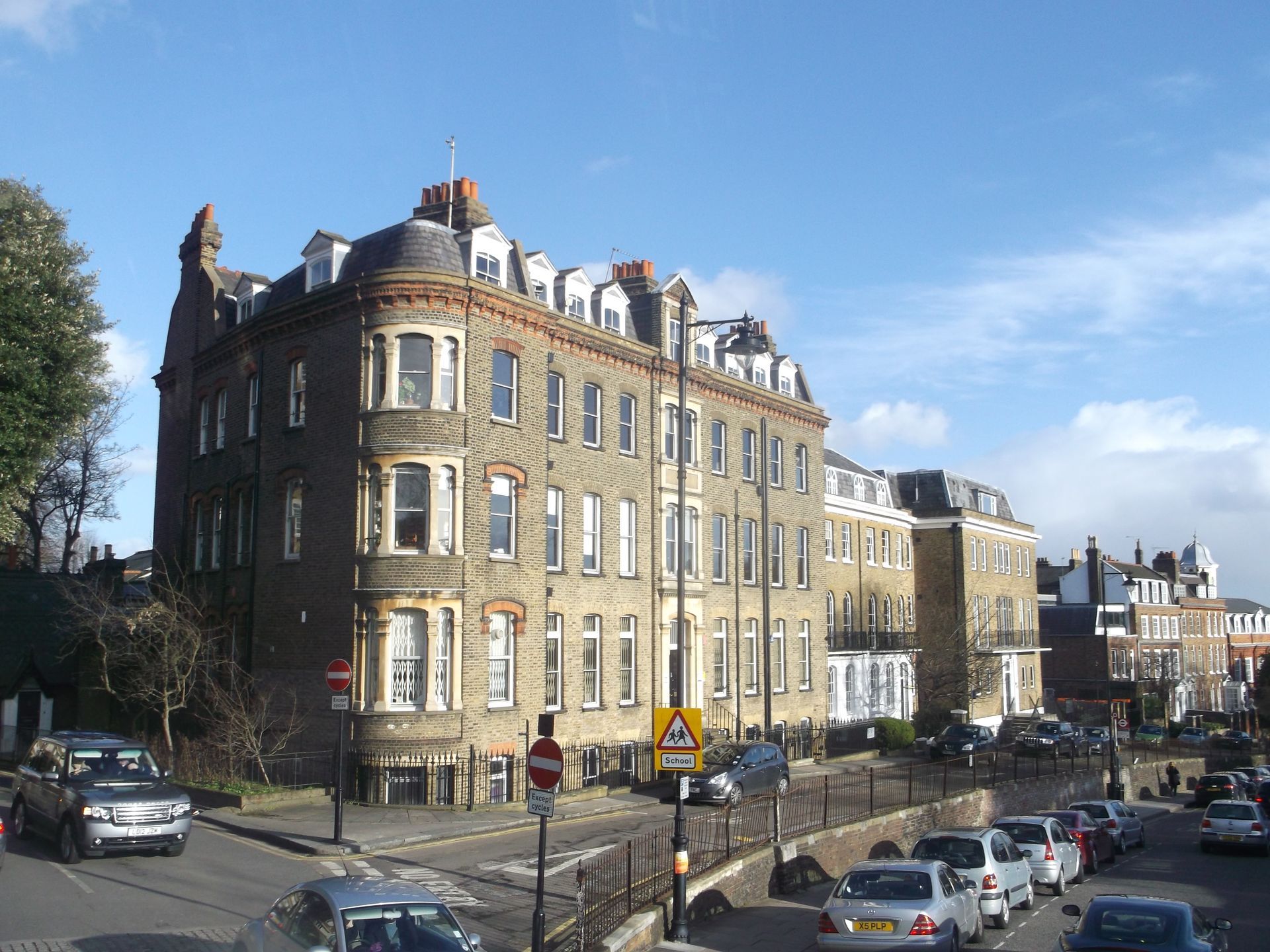 A multi-story building with a curved corner on a street with cars. The building is brick with many windows.