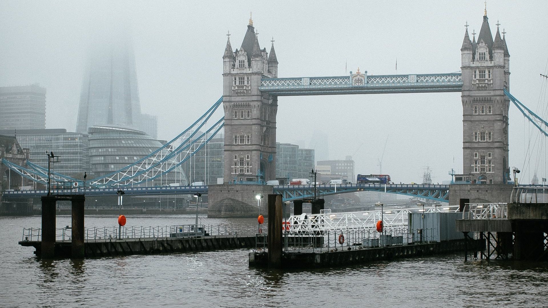 Tower Bridge in London on a cloudy day; a river flows in front of the bridge.