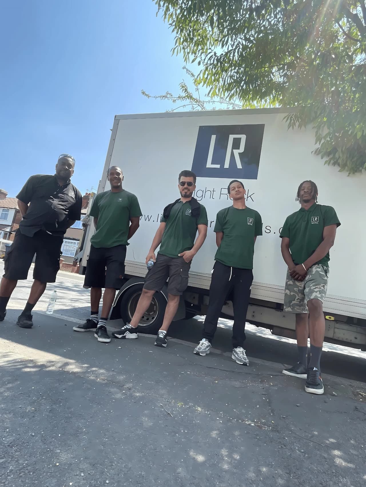 Five movers in green shirts stand in front of a white truck with
