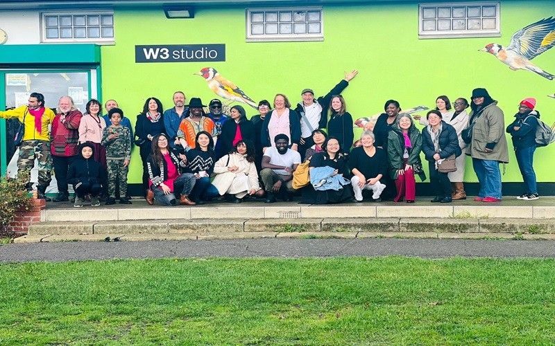 Group of diverse people outside W3 studio, posed in front of a mural with green and bird imagery.