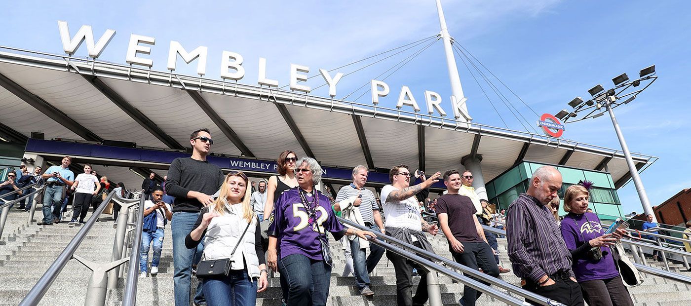 People walking down stairs at Wembley Park stadium under a sunny sky. Some are wearing sports jerseys.