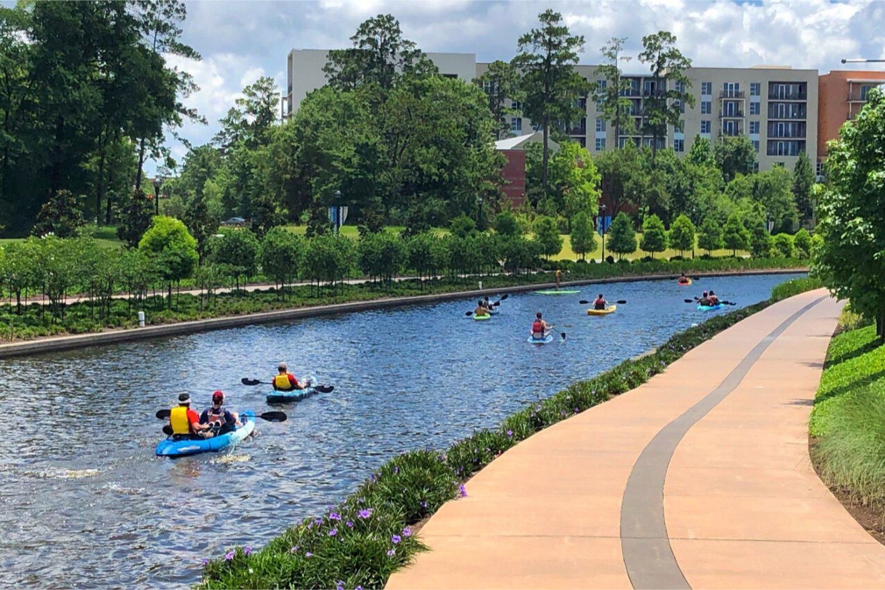 A group of people are rowing kayaks down a river in The Woodslands.