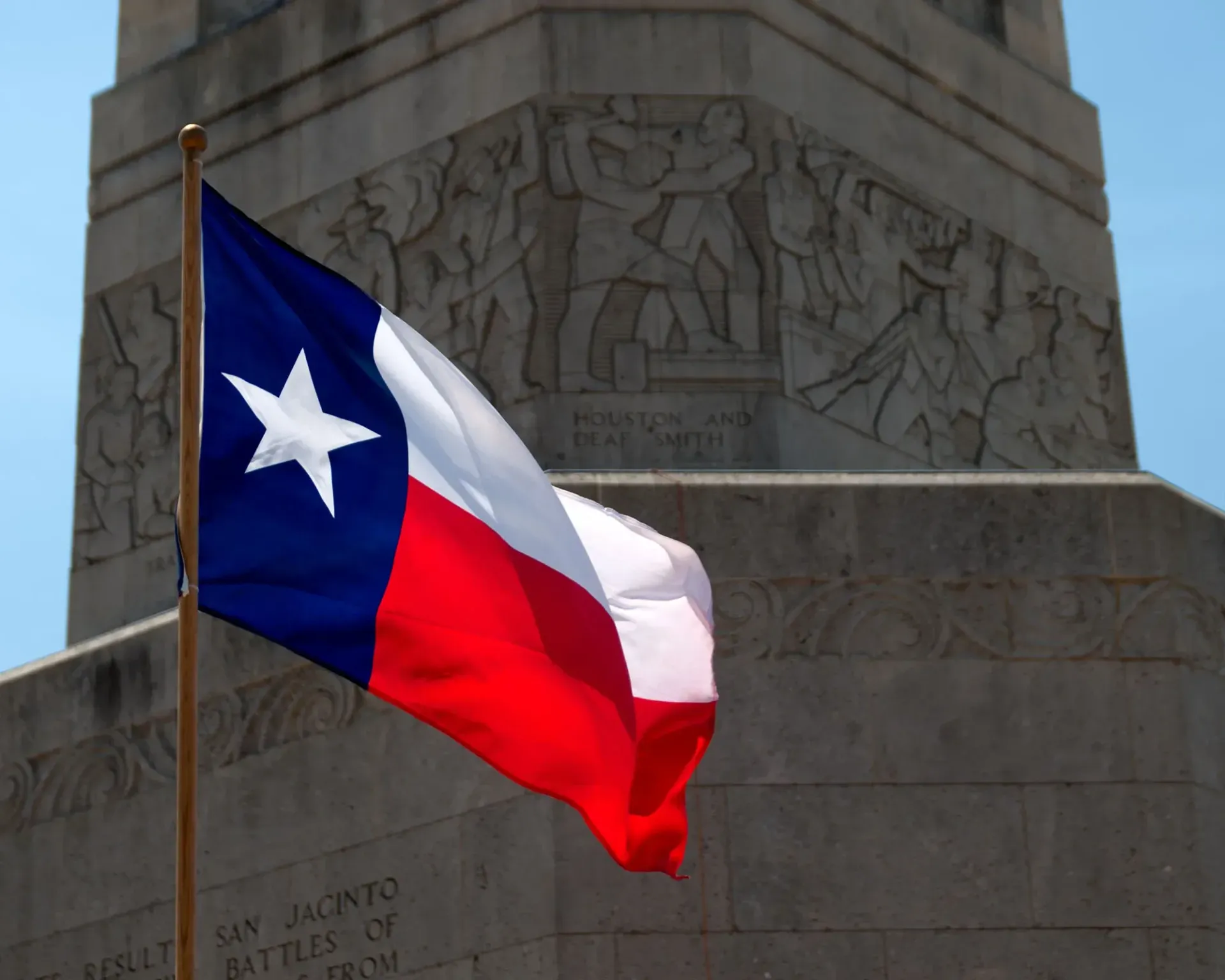 A Texas flag is flying in front of a monument in Houston.