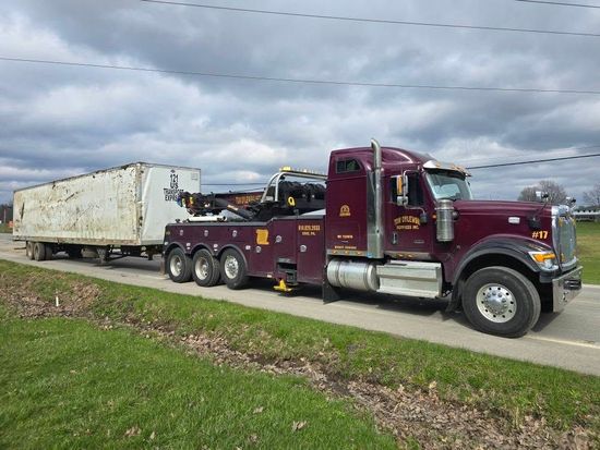A red tow truck is towing a tractor in a field A red tow truck is towing a tractor in a field