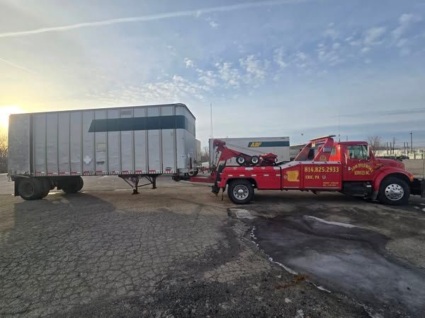 A white truck is being towed by a crane on the side of the road. A white truck is being towed by a crane on the side of the road.
