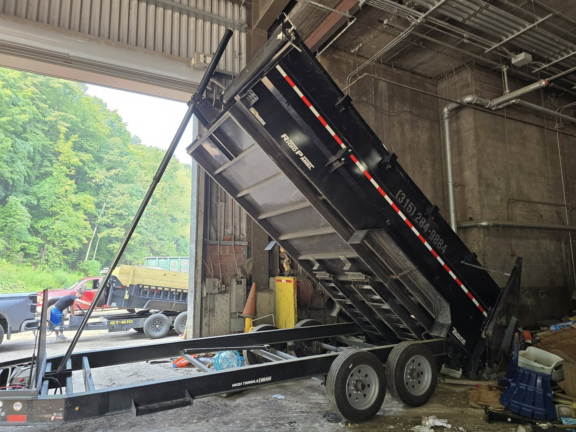 Black dump trailer with raised bed inside a building with a large open doorway.