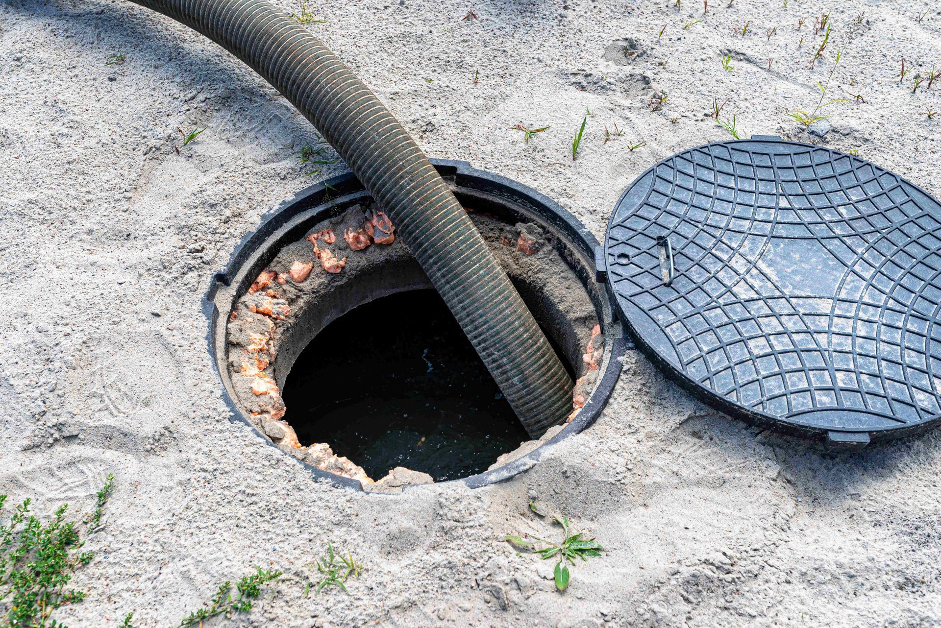 Open manhole in concrete with a hose and a round metal cover beside it