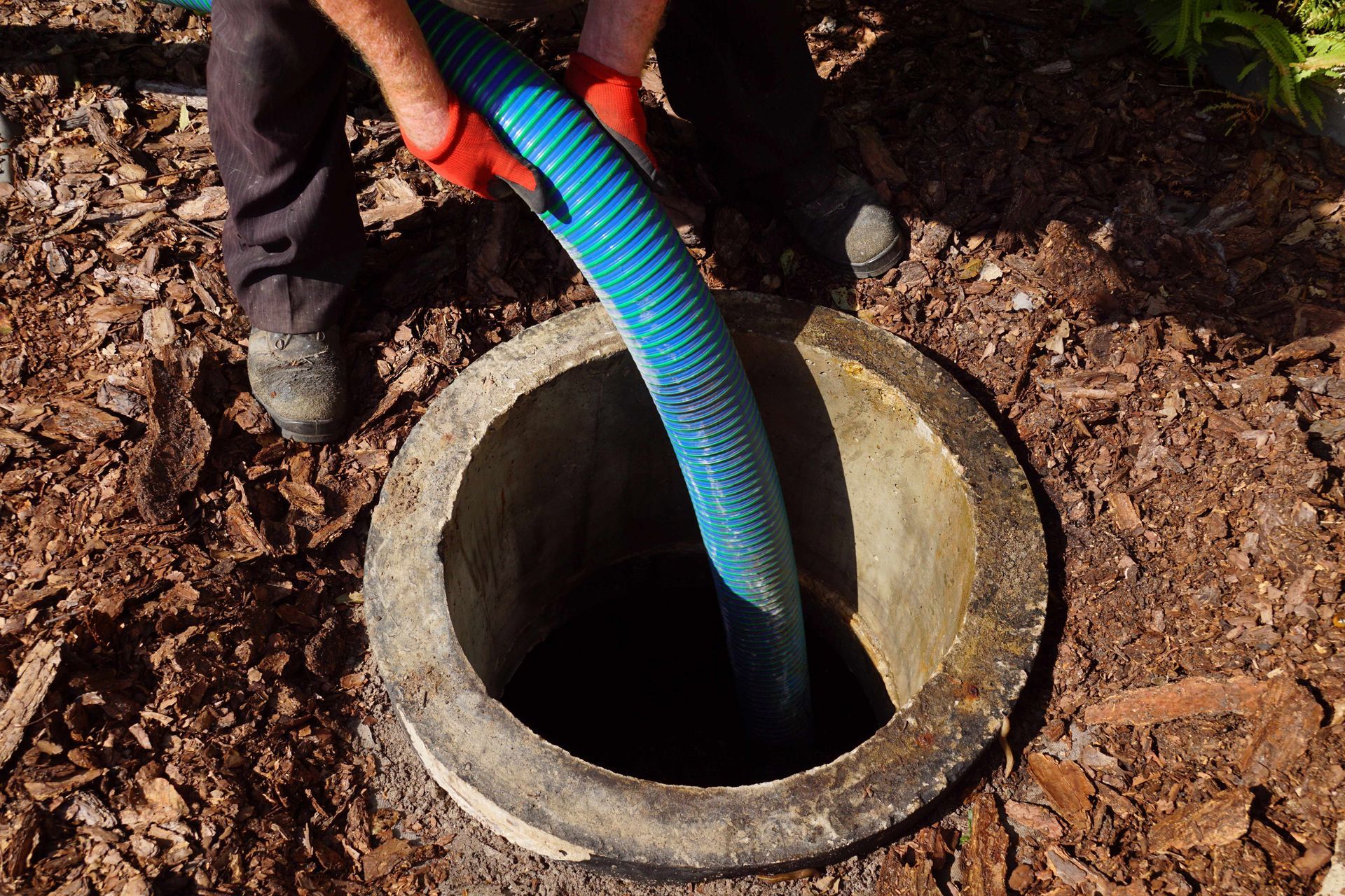 Person pours a blue hose into a round concrete well in a dirt-covered outdoor area