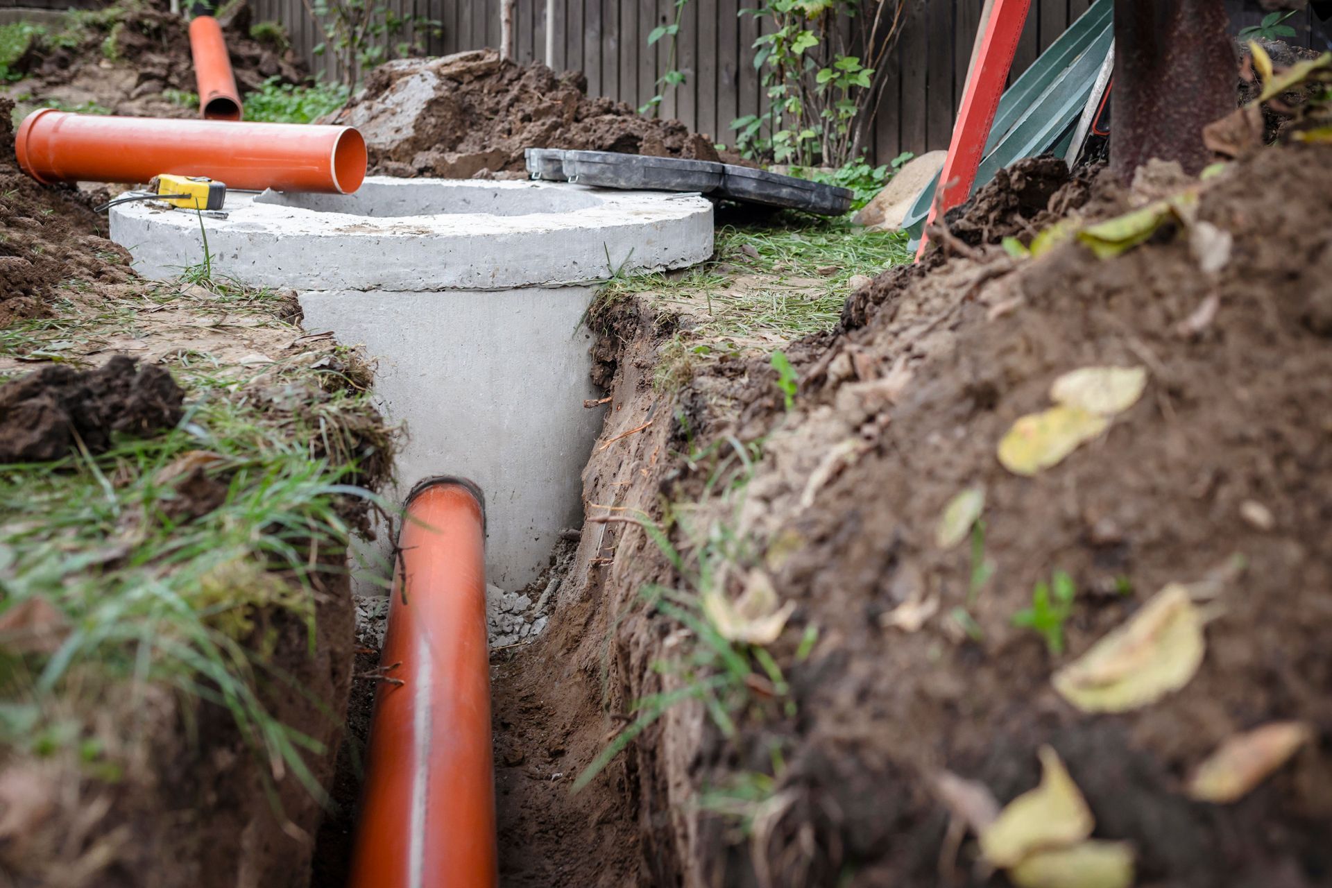 Orange pipes running through a narrow backyard trench around a concrete utility box.