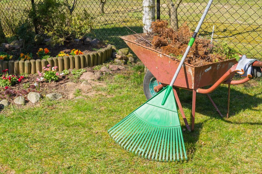 A green rake is sitting next to a wheelbarrow filled with dirt.