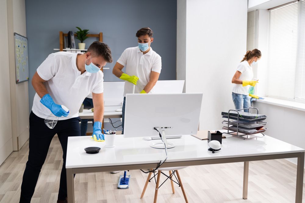 A group of people wearing masks and gloves are cleaning an office.