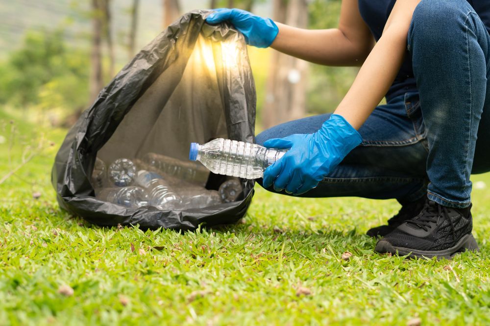A person wearing blue gloves is picking up plastic bottles from a trash bag.