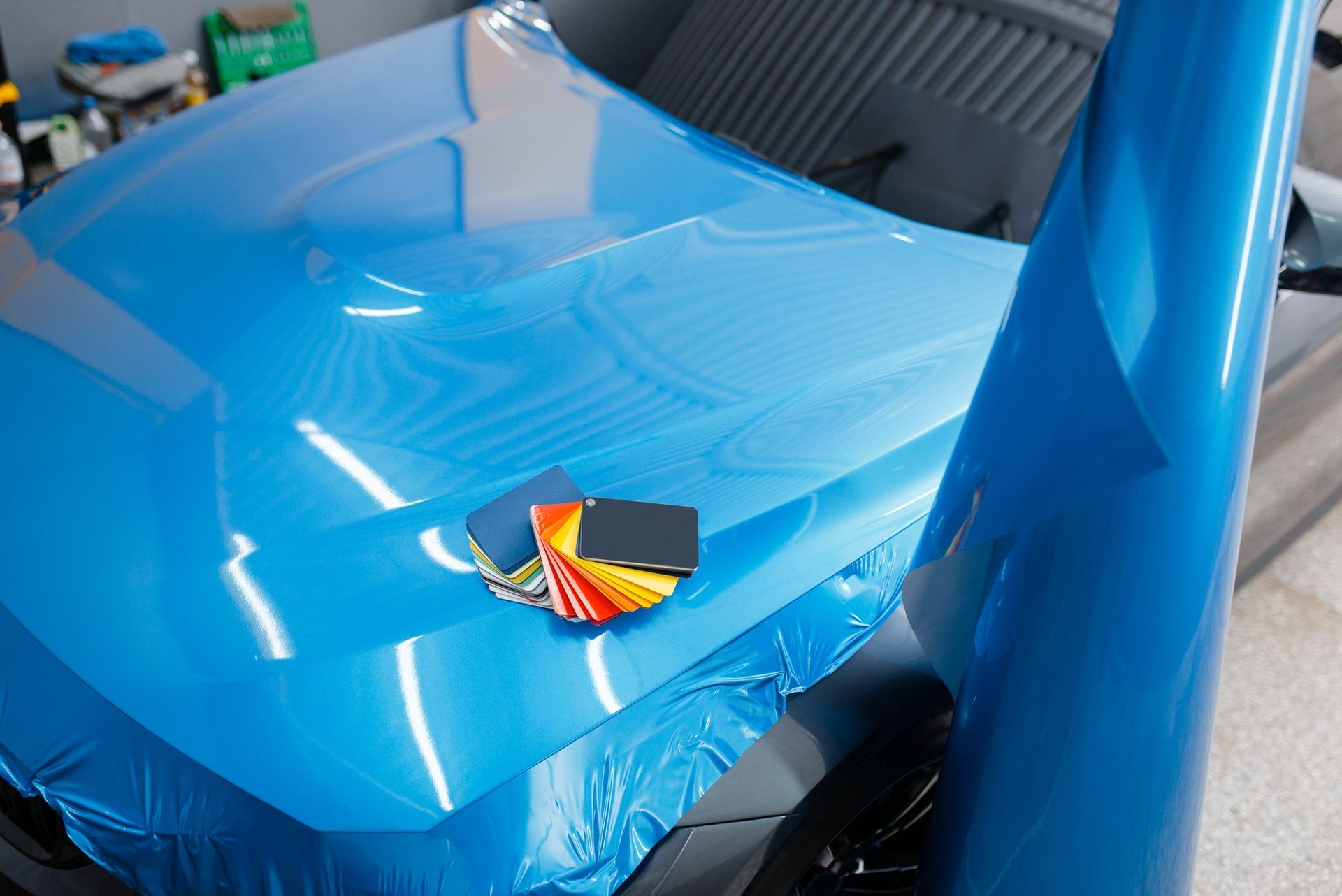 A bright blue car hood being wrapped in vinyl, with a color swatch fan held in the center.