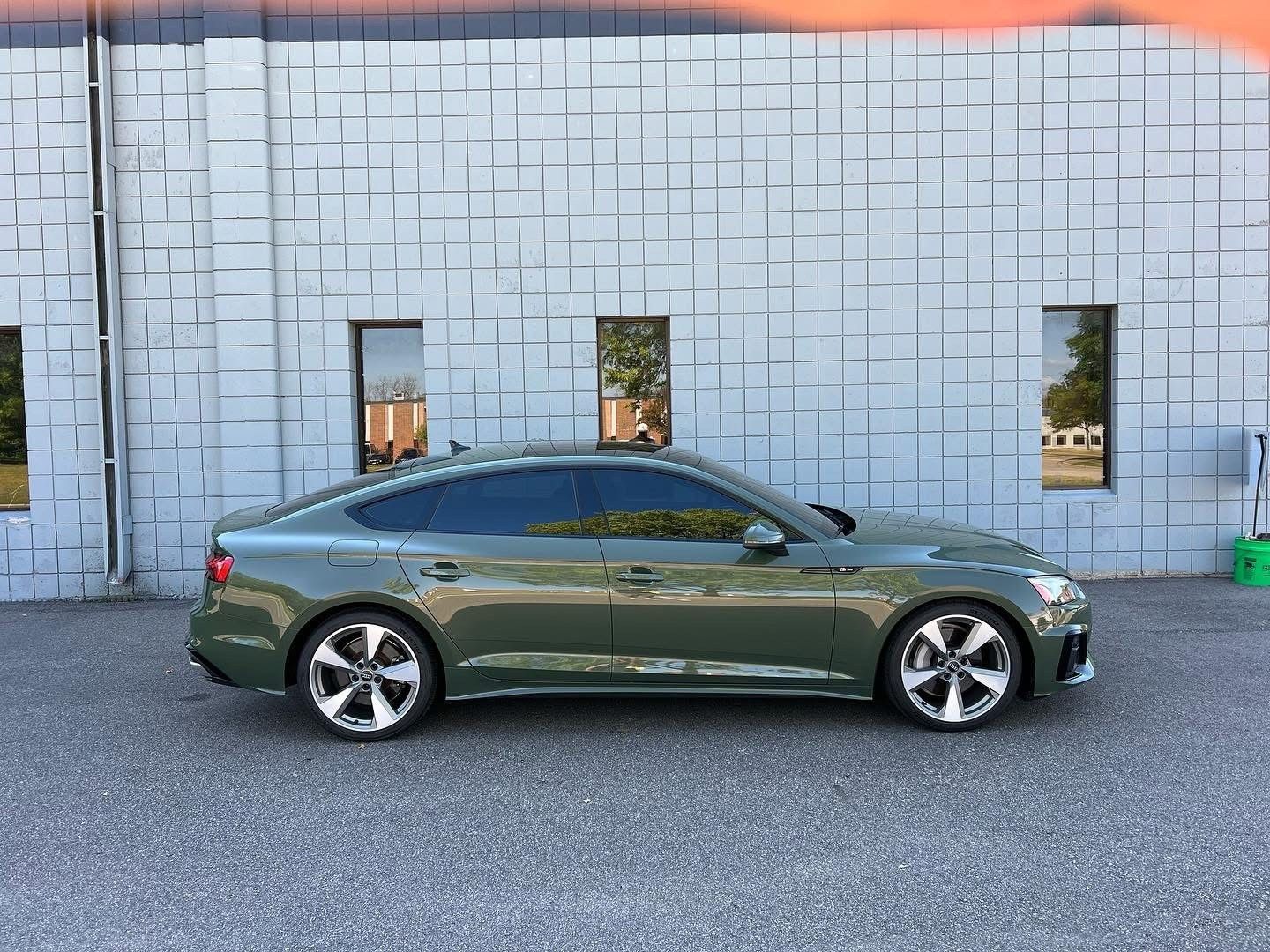 Green sports sedan parked in front of a light gray brick wall with two windows.