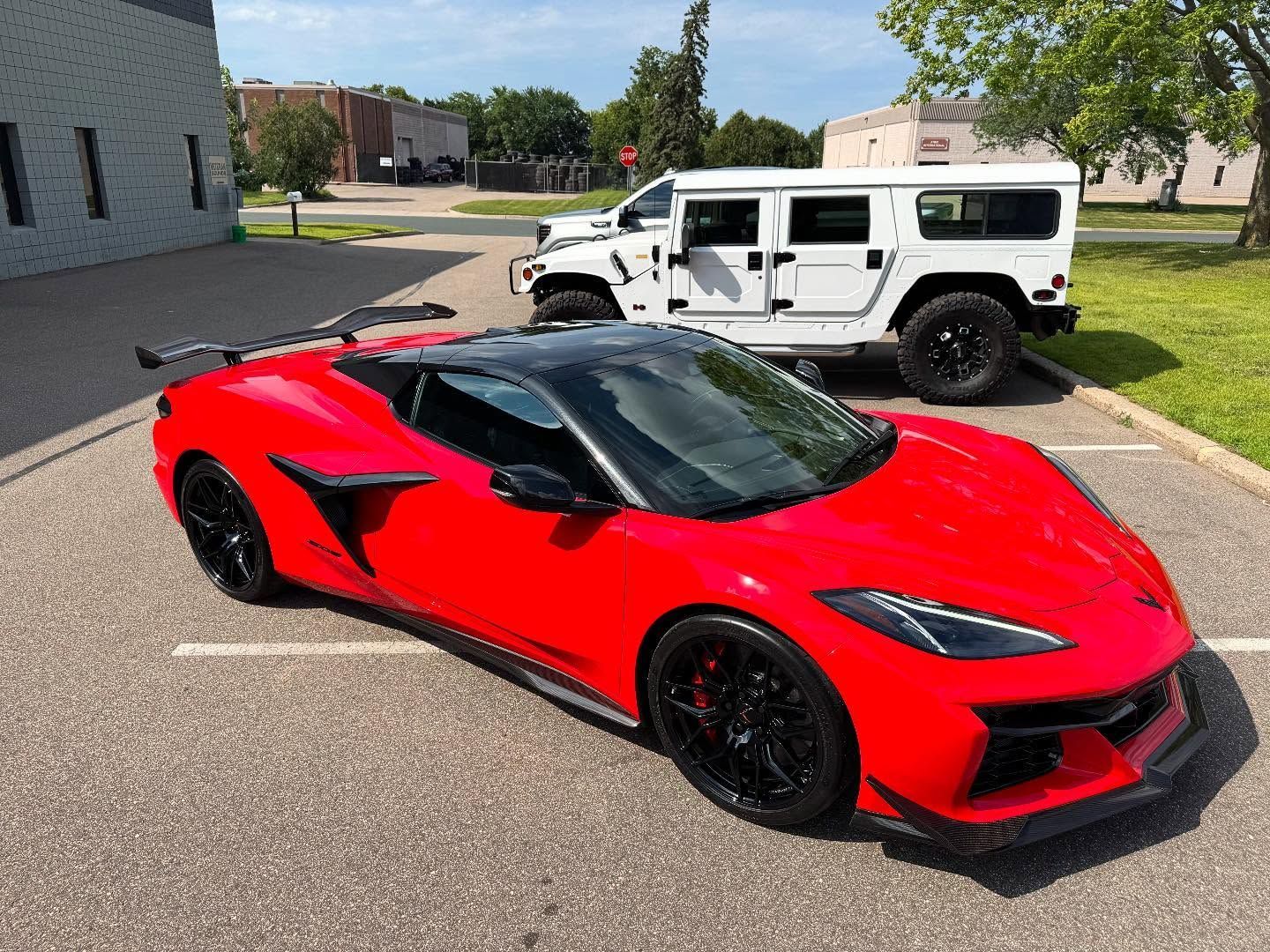 A red Chevrolet Corvette Z06 convertible parked next to a white Hummer in a sunny outdoor lot.