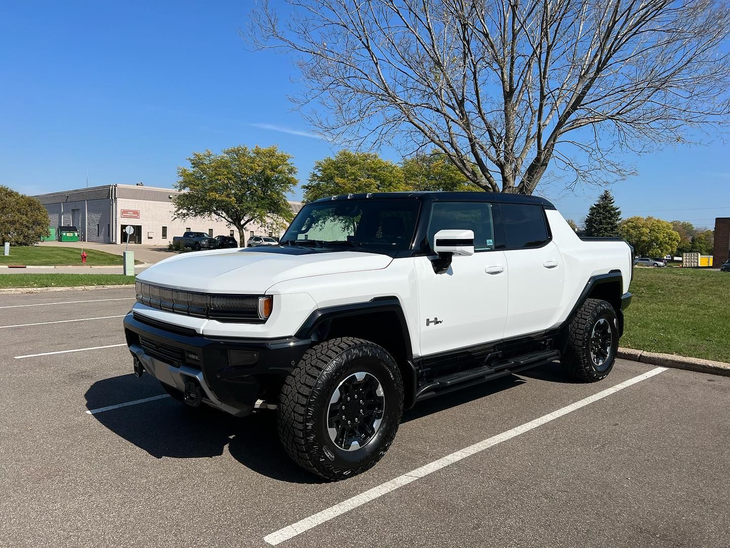 A white GMC Hummer EV pickup truck parked in an outdoor parking lot on a sunny day.