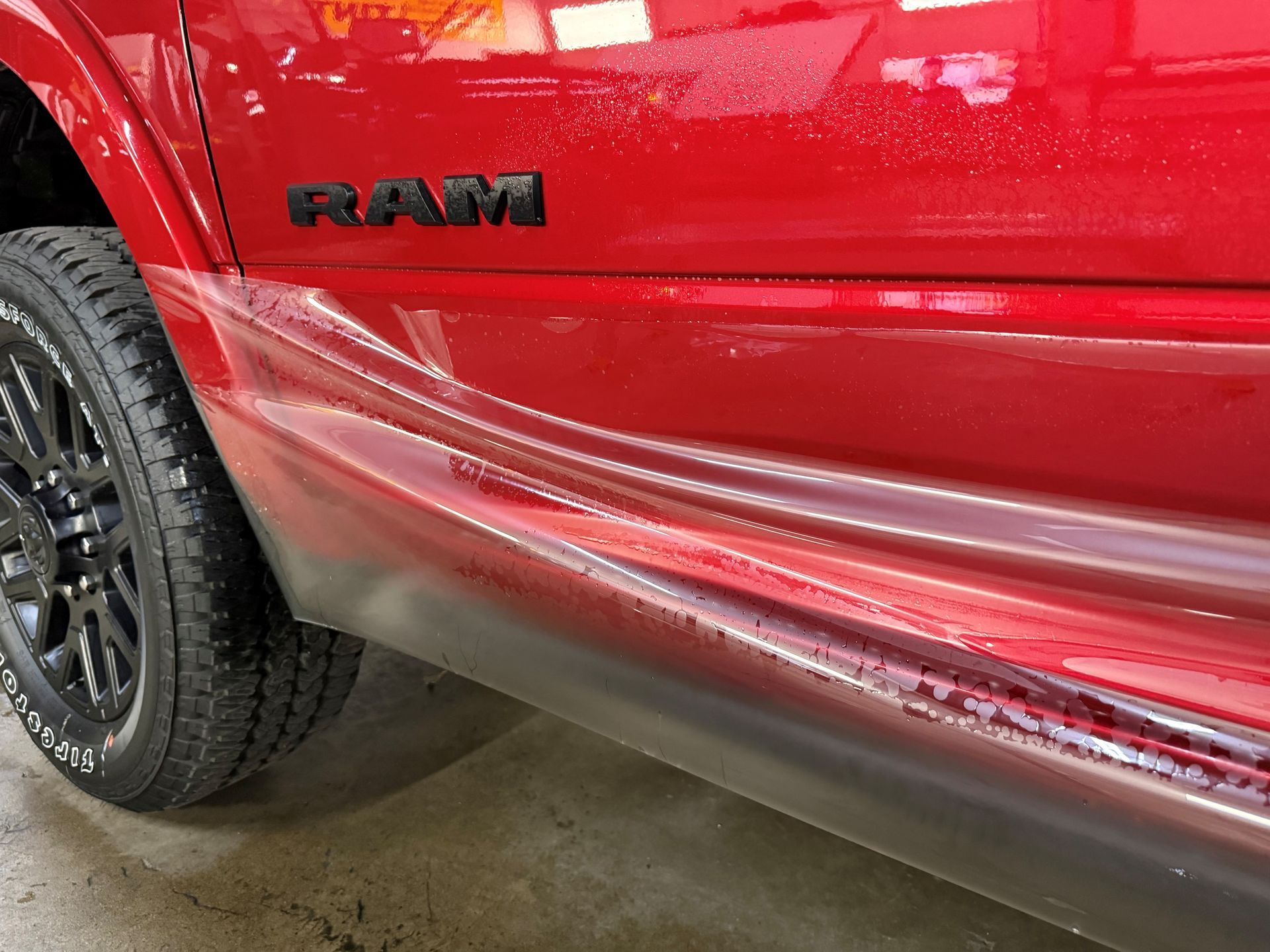 Close-up of a red RAM truck with a scratched and dented side panel near the rear wheel