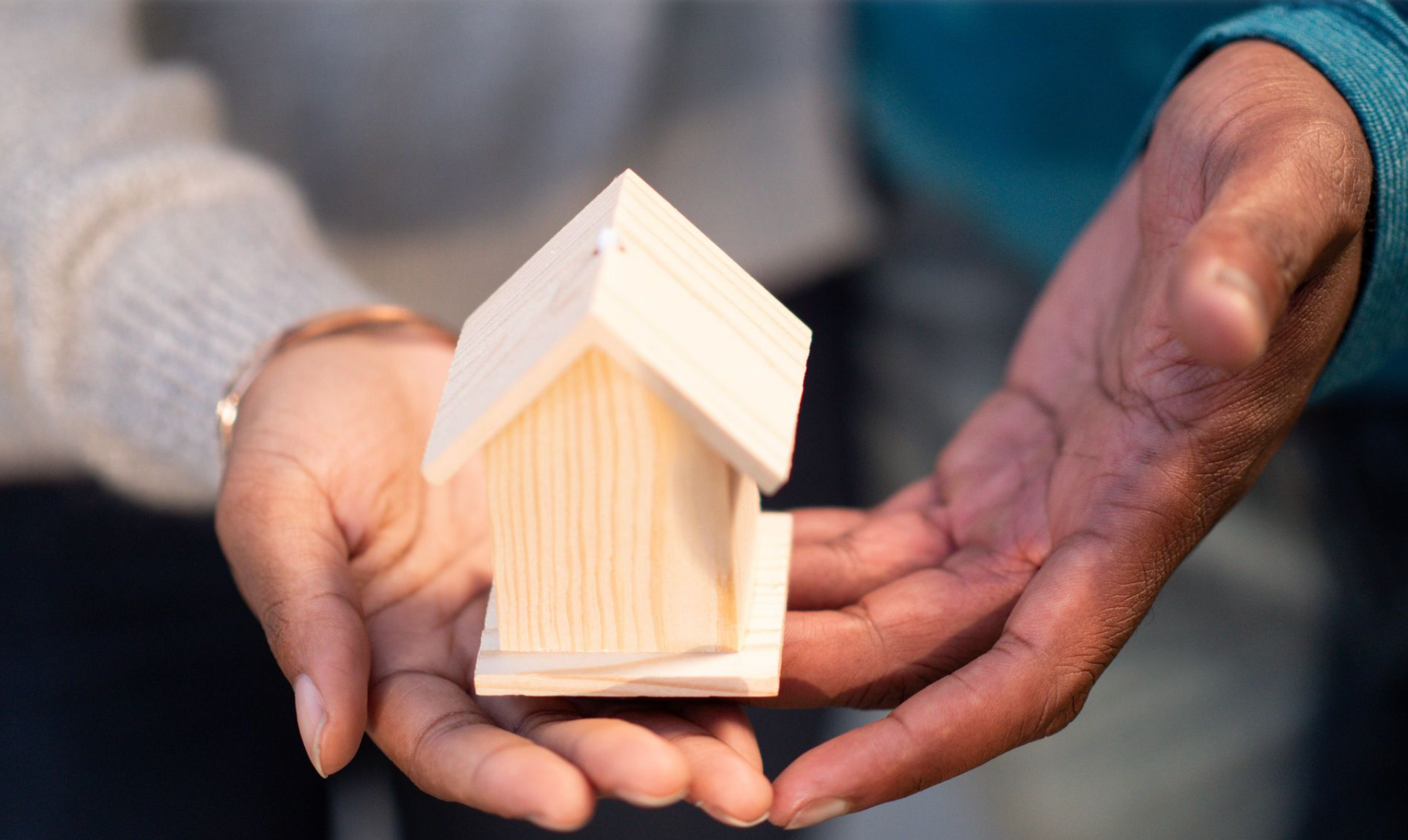 Two people holding a miniature wooden house together, representing senior partnerships and teamwork