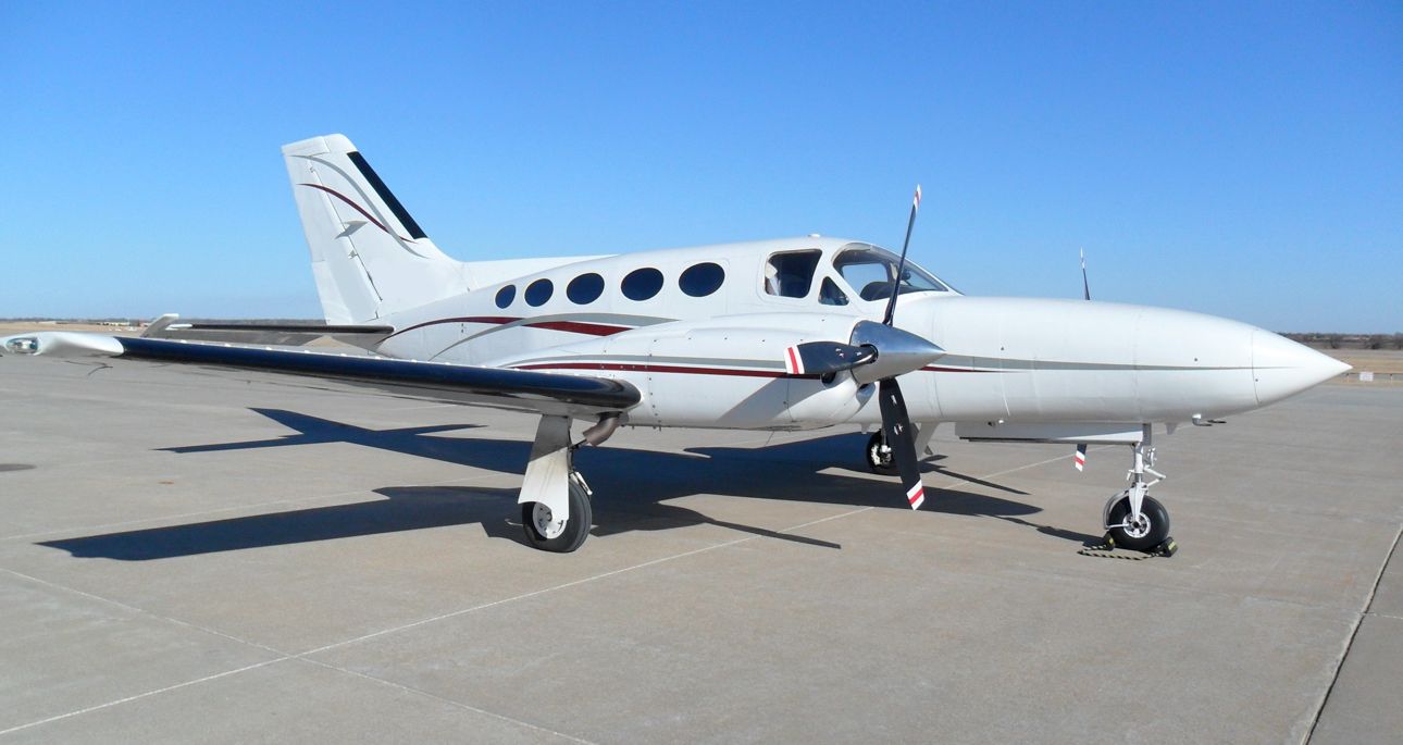 White twin-engine airplane parked on a tarmac under a clear blue sky.