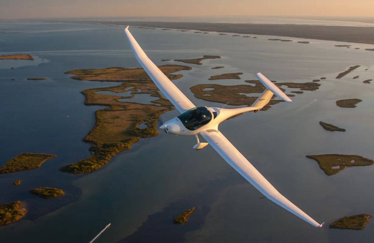 White glider soaring above a coastal landscape, reflecting sunlight on its wings.