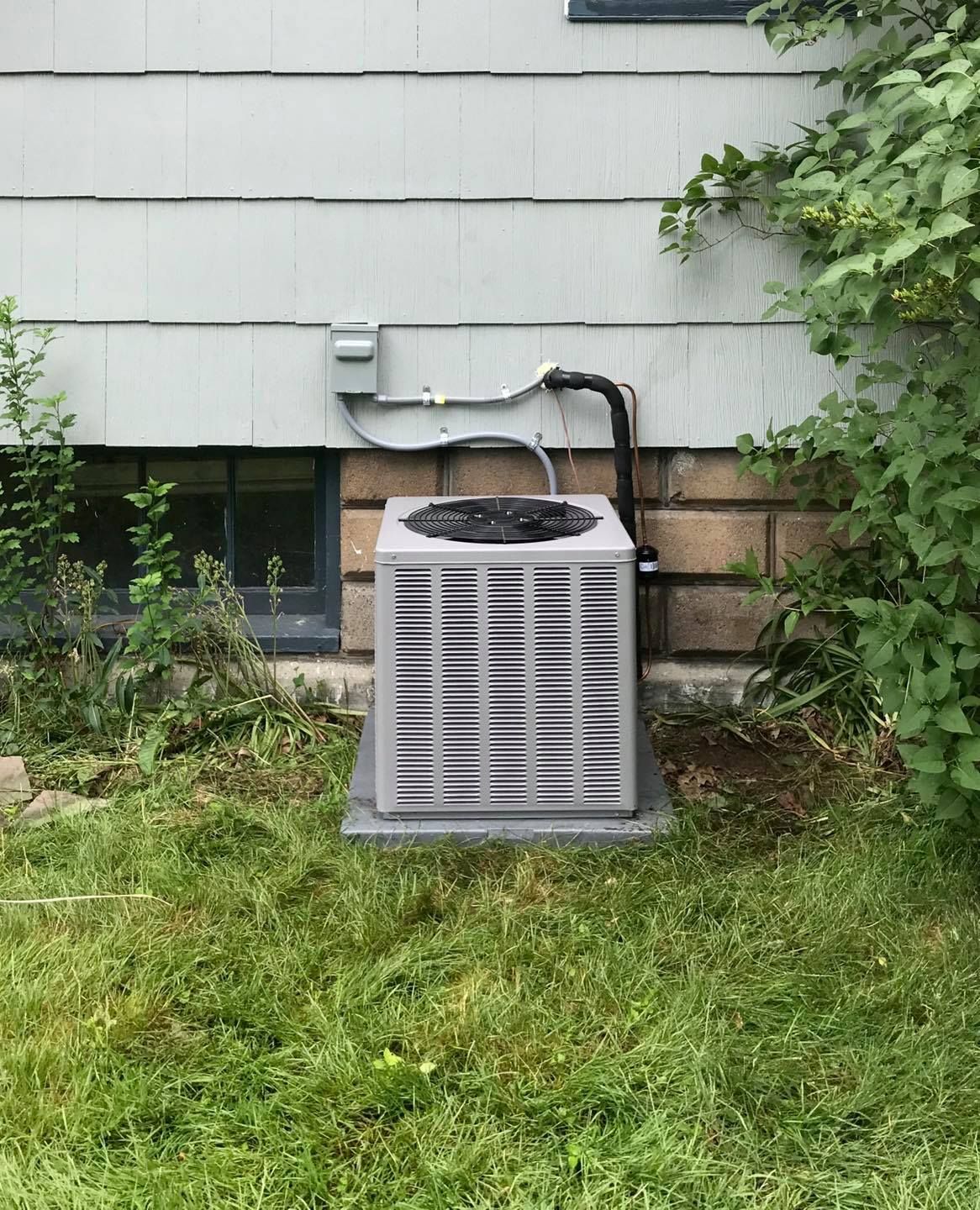 An air conditioner is sitting in the grass in front of a house.