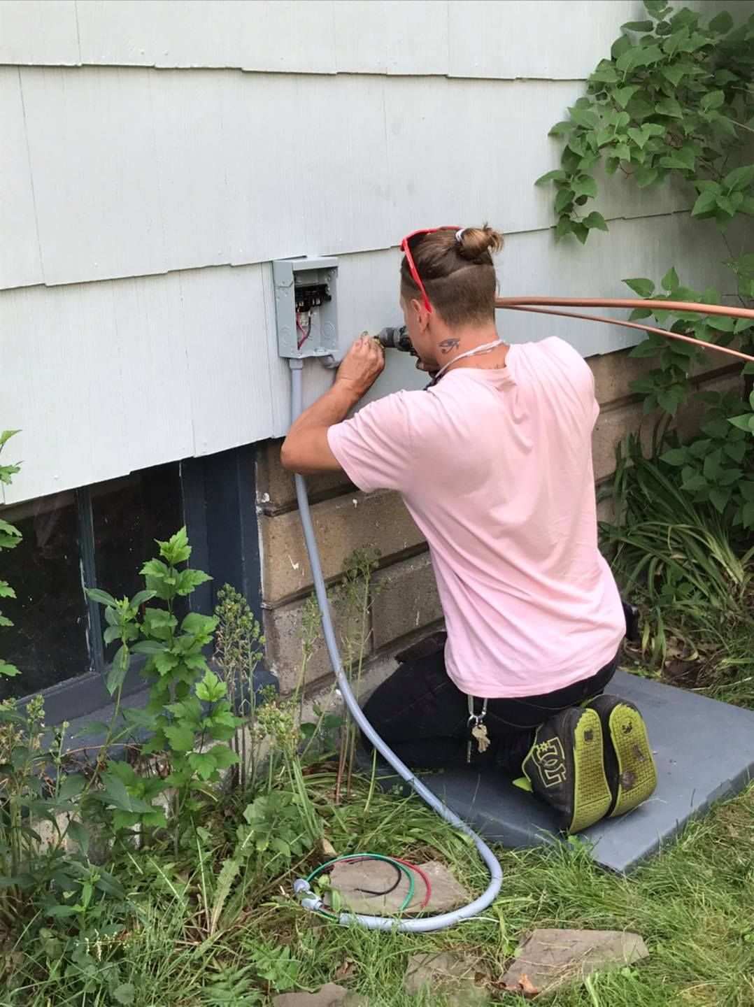 A man is kneeling down in front of a house working on an electrical box.