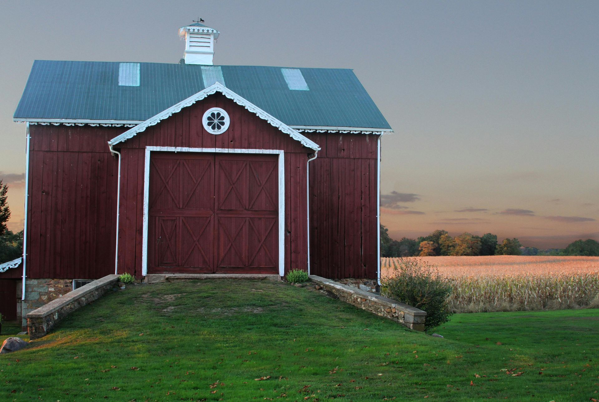 Red barn with white trim and large double doors in a grassy field at sunset