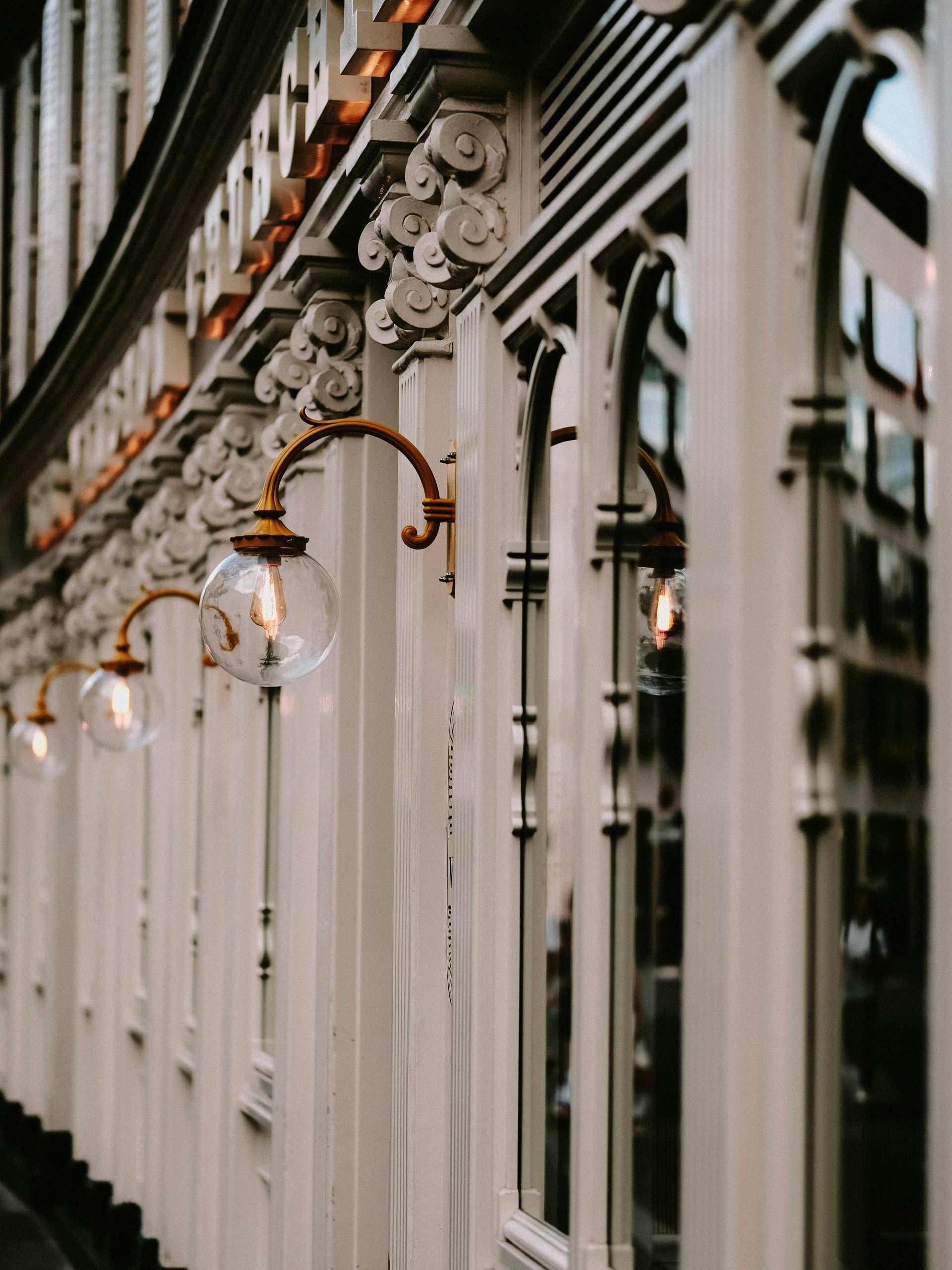 Row of ornate white building facades with arched windows and bronze wall lamps