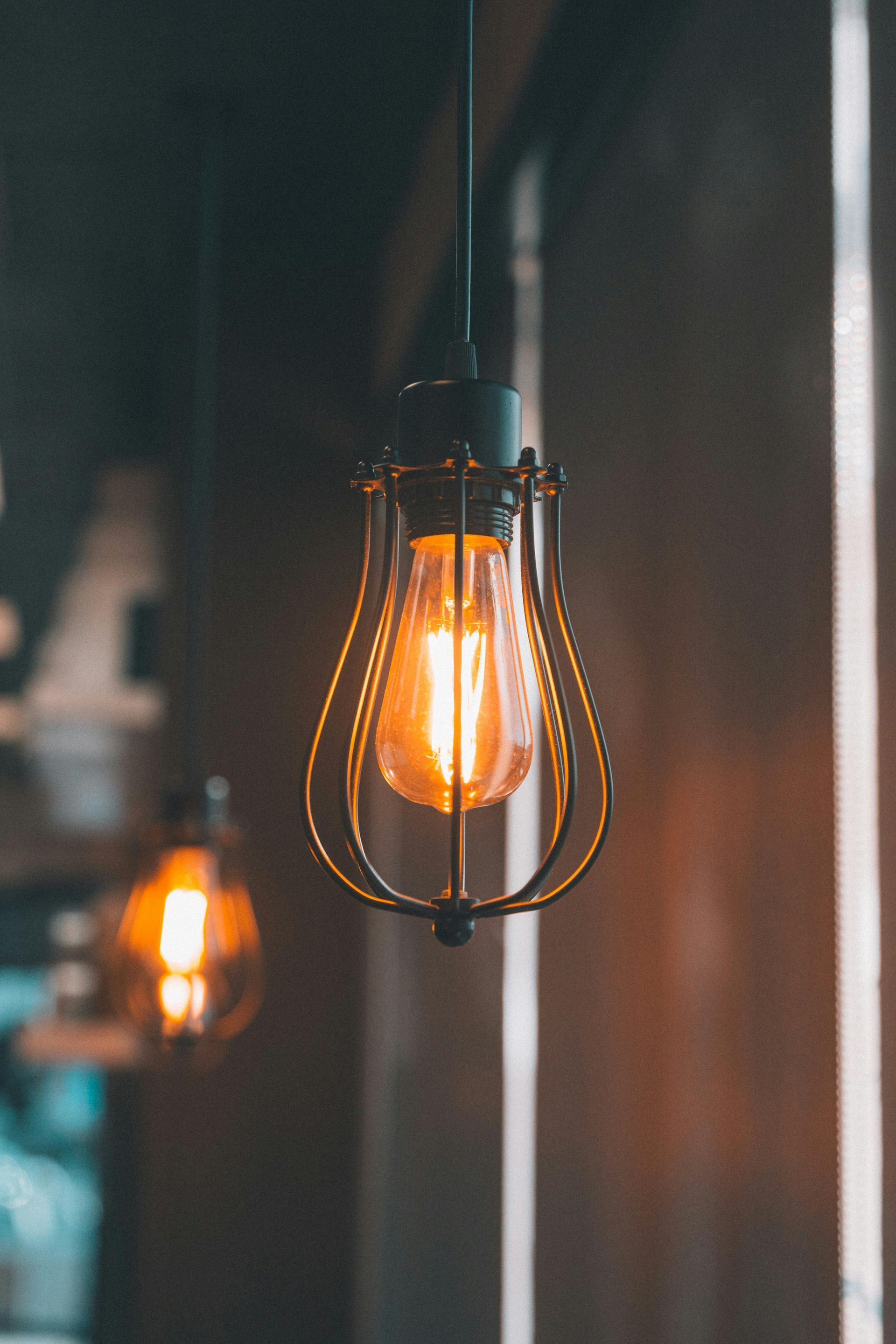 Warm glowing bulb in a vintage wire cage, hanging indoors against a blurred dark background