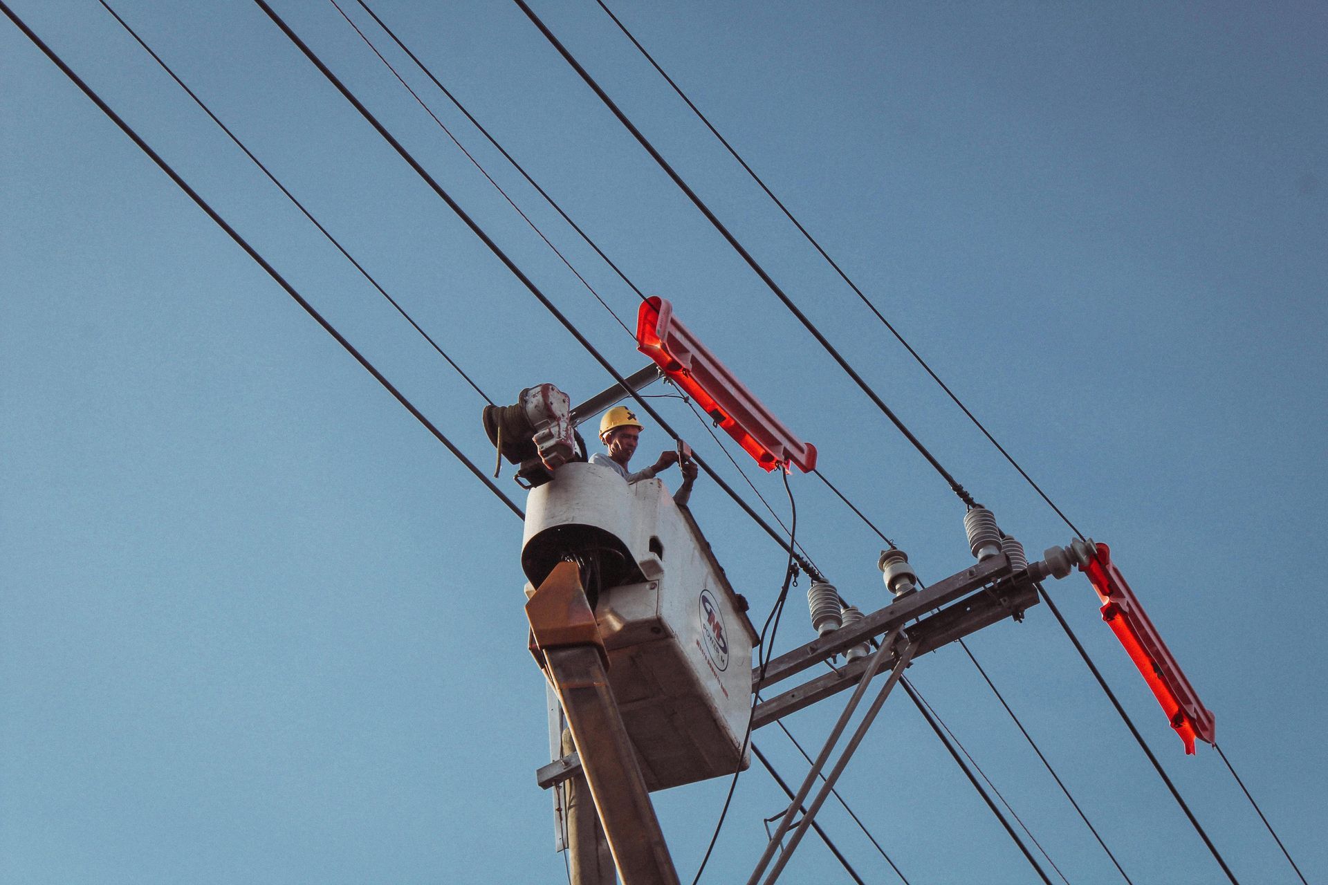 Utility worker in a bucket lift repairing overhead power lines against a blue sky