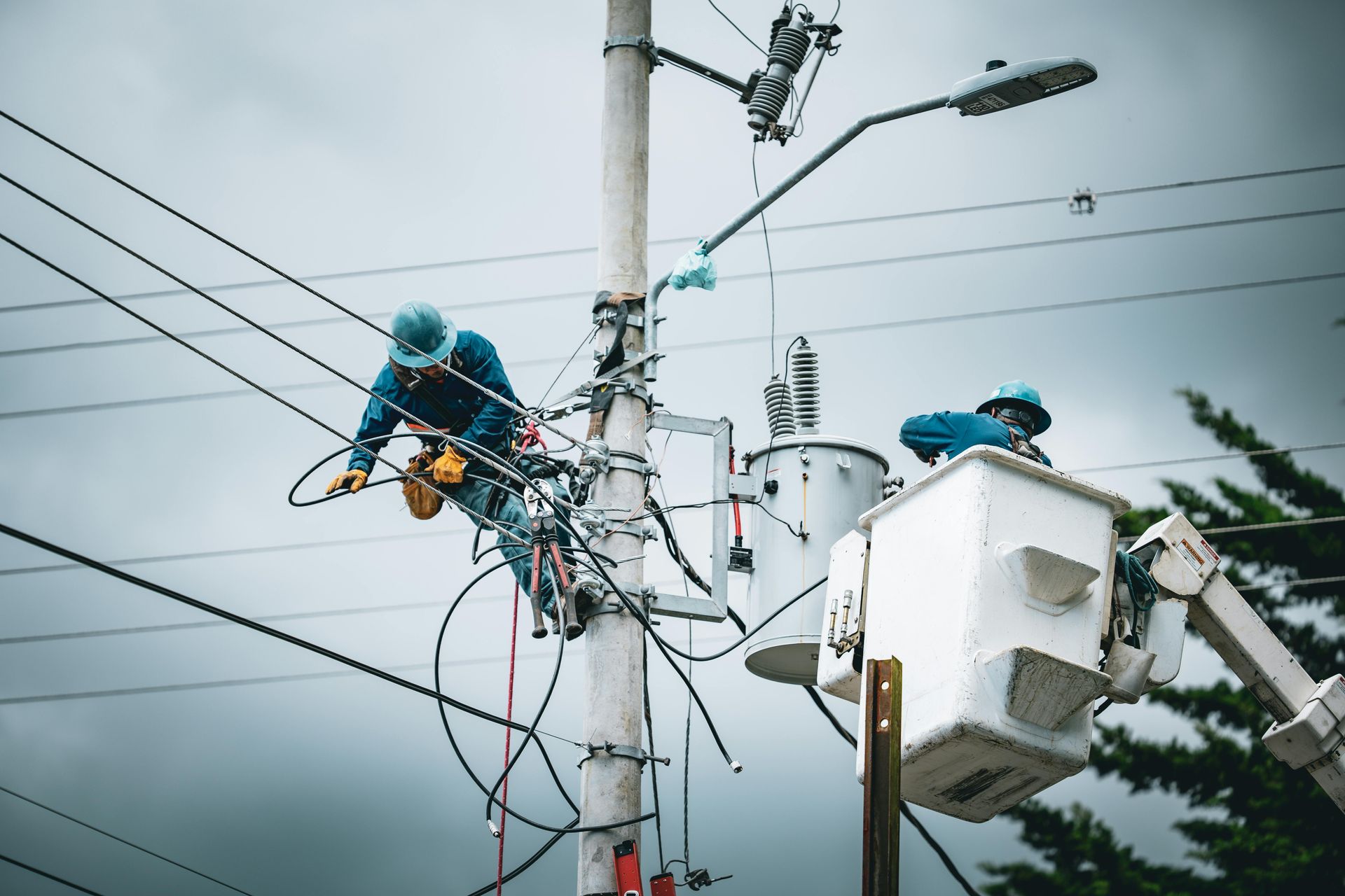 Utility workers in blue uniforms repairing power lines on a pole from bucket trucks