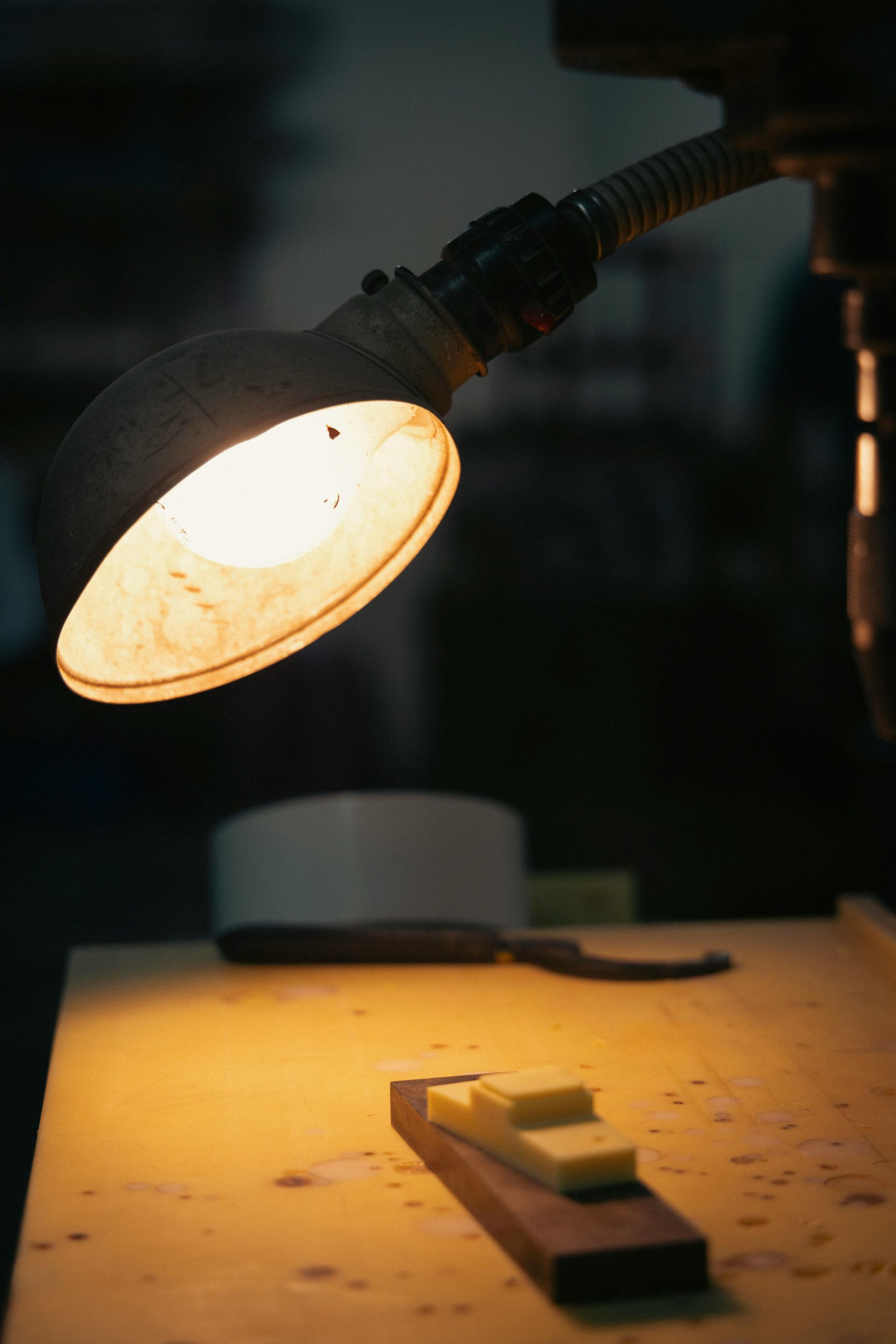 Desk lamp shining on a workbench with scattered papers and a ruler at the bottom.