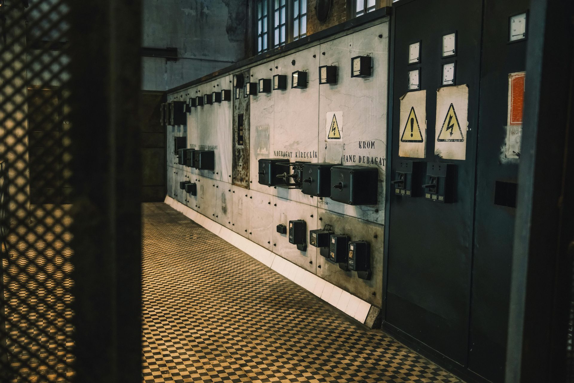 Industrial electrical control panels along a wall in a dimly lit room with patterned flooring.