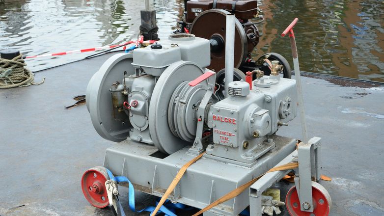Gray industrial pump/motor unit mounted on a wheeled frame in shallow water, with hoses attached